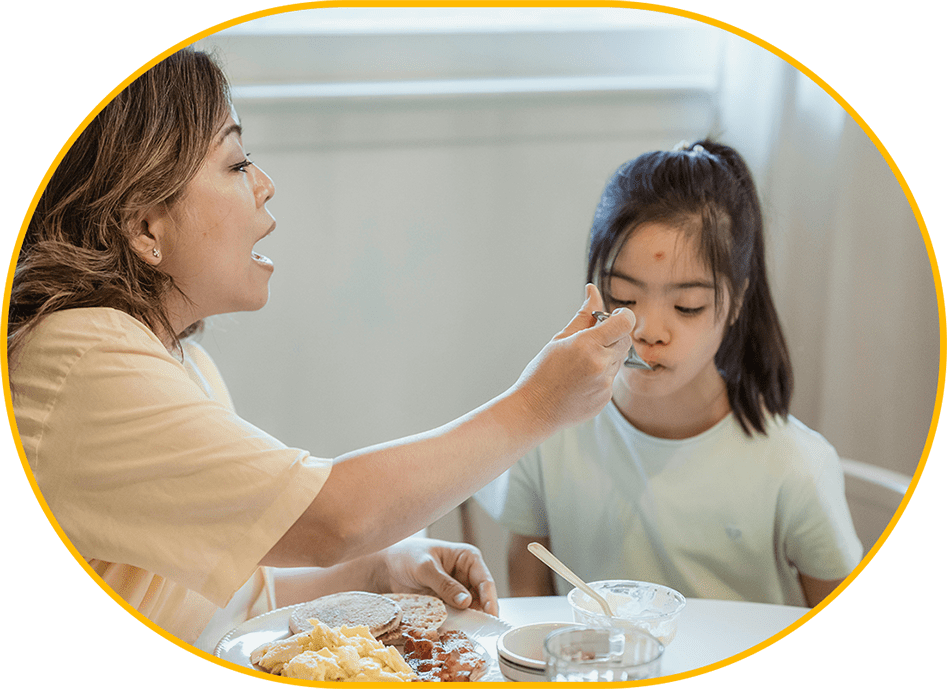 A woman feeding food to a child at the table.